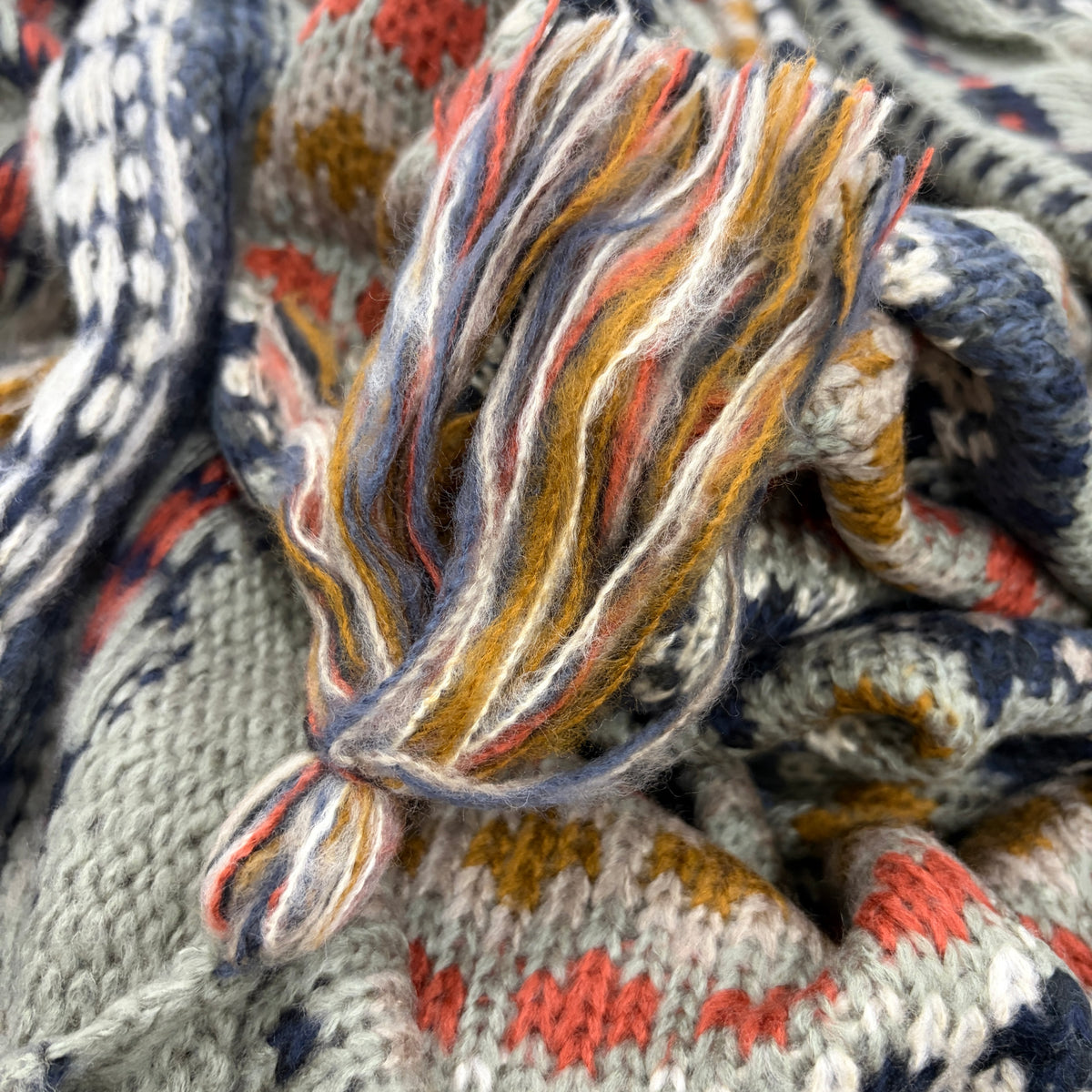 Close-up detail of Nordic Grey Wrap tassel fringe in mixed navy, mustard, coral and sage threads