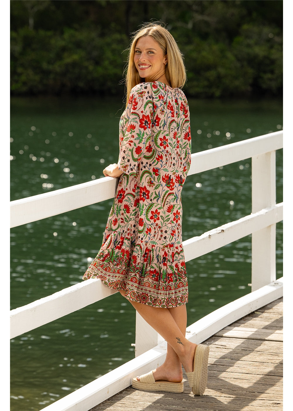 Ada Carmen Dress in pink floral cotton, three-quarter back view beside the water