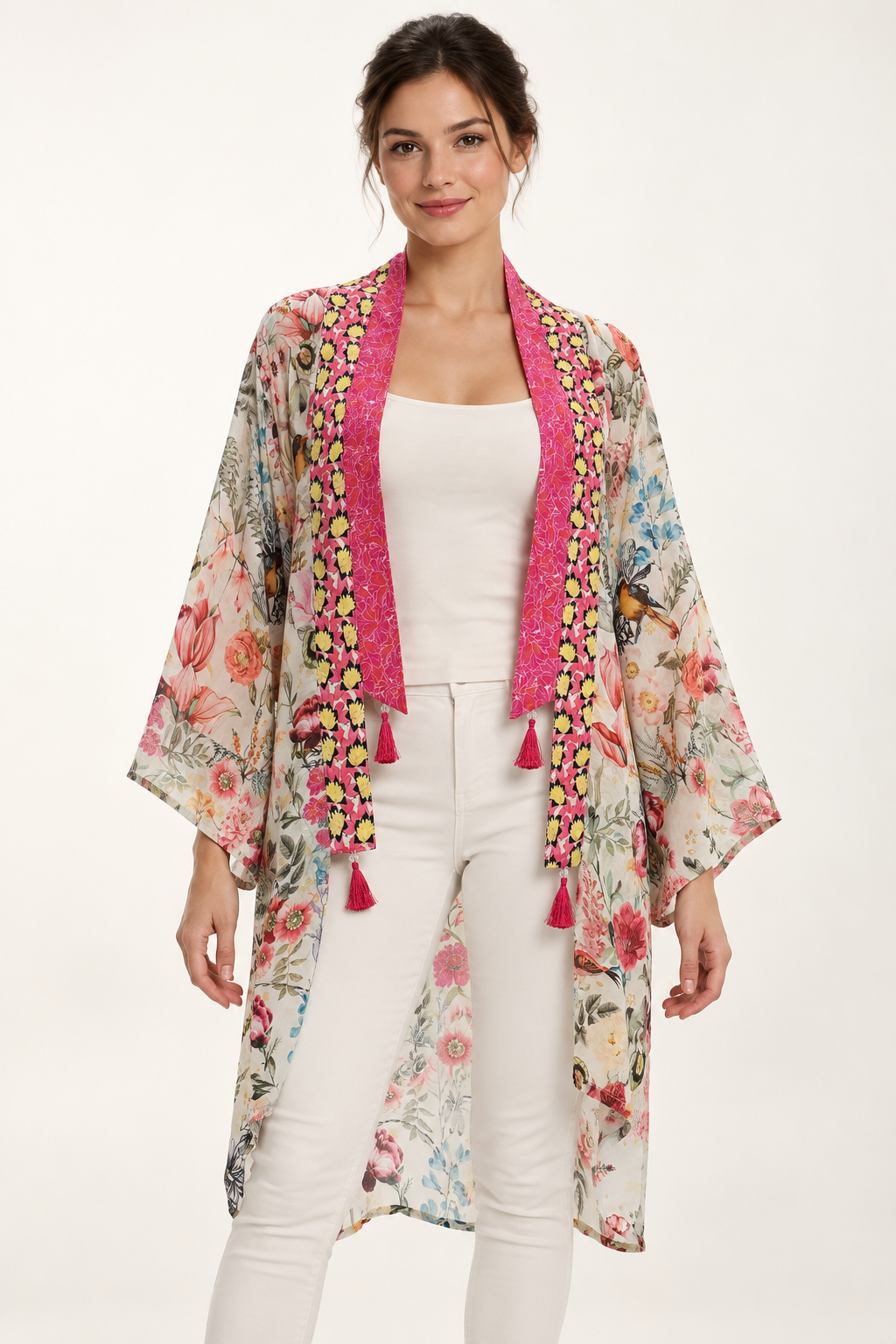 Birdsong Kimono in an ivory bird and floral print with pink borders and tassels, front view worn over a white top and trousers