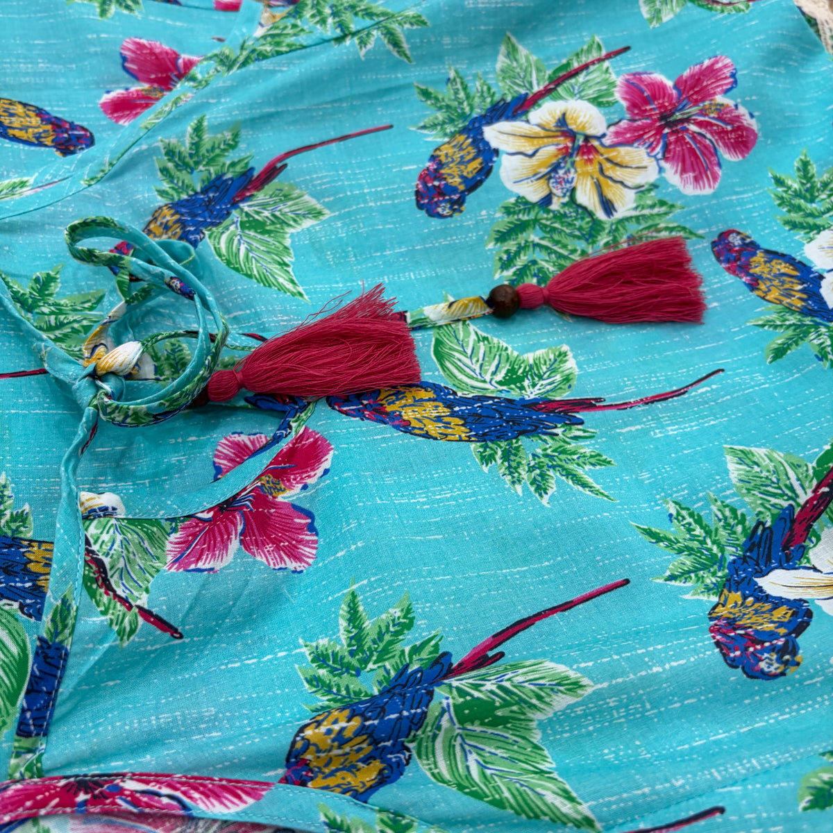 CJ-165 Bird Long Dress in turquoise blue cotton, close view of the magenta tassel ties and parrot print fabric