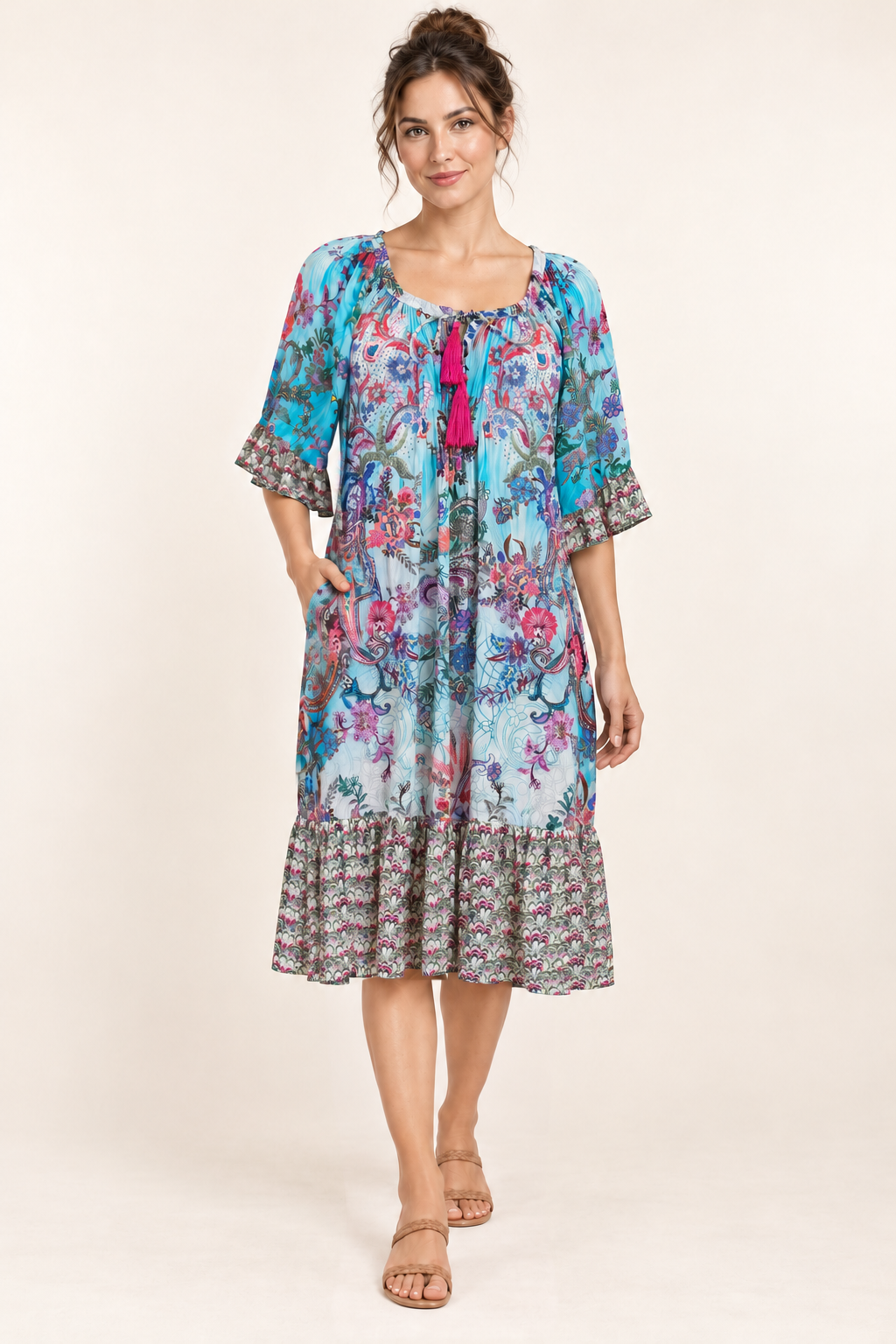 Turquoise Rhapsody Frill Dress, a blue floral and paisley viscose rayon dress, studio front view with a hand in the side pocket.