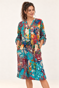 Zahara Dress in turquoise floral and paisley print, worn loose with sleeves rolled up and both hands in the side pockets.