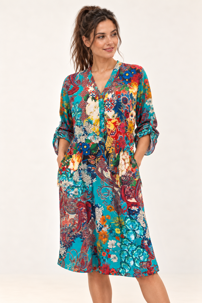 Zahara Dress in turquoise floral and paisley print, worn loose with sleeves rolled up and both hands in the side pockets.