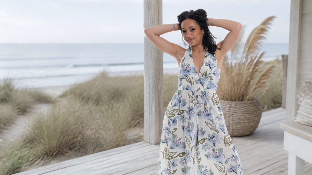 Haven Halter Jumpsuit in cream with blue floral print and wide legs, worn on a beach deck