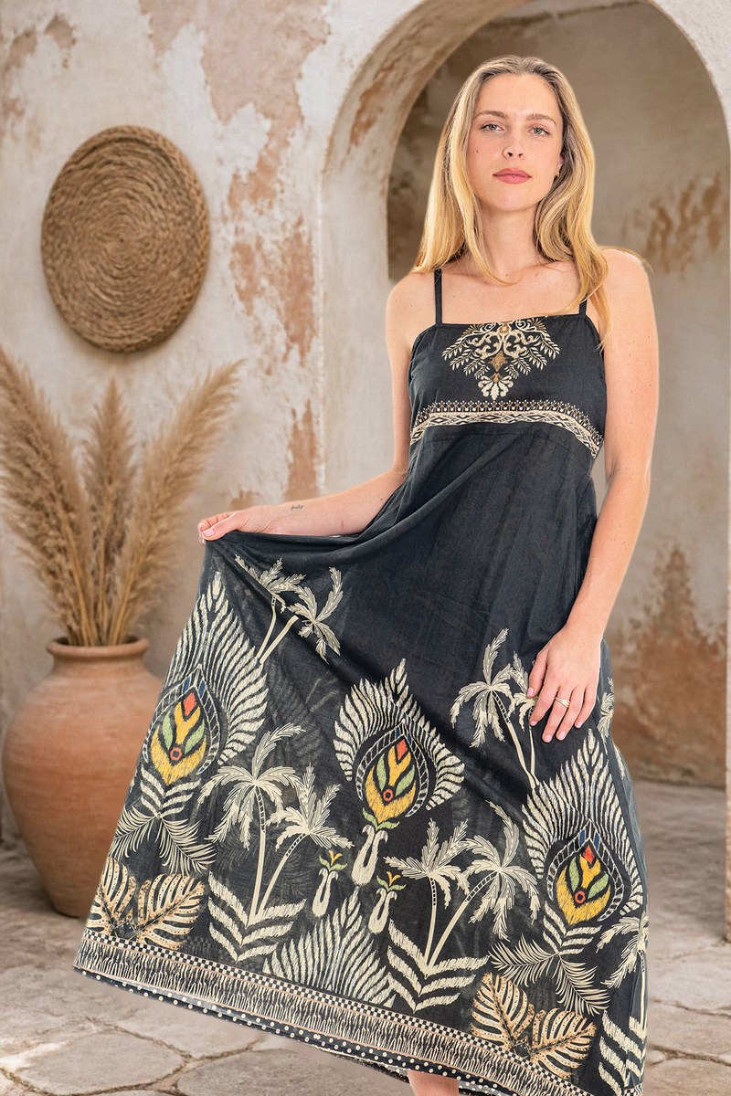 Malie Mood Dress, a black strappy maxi dress with gold and cream palm-leaf print, worn in a sunlit courtyard
